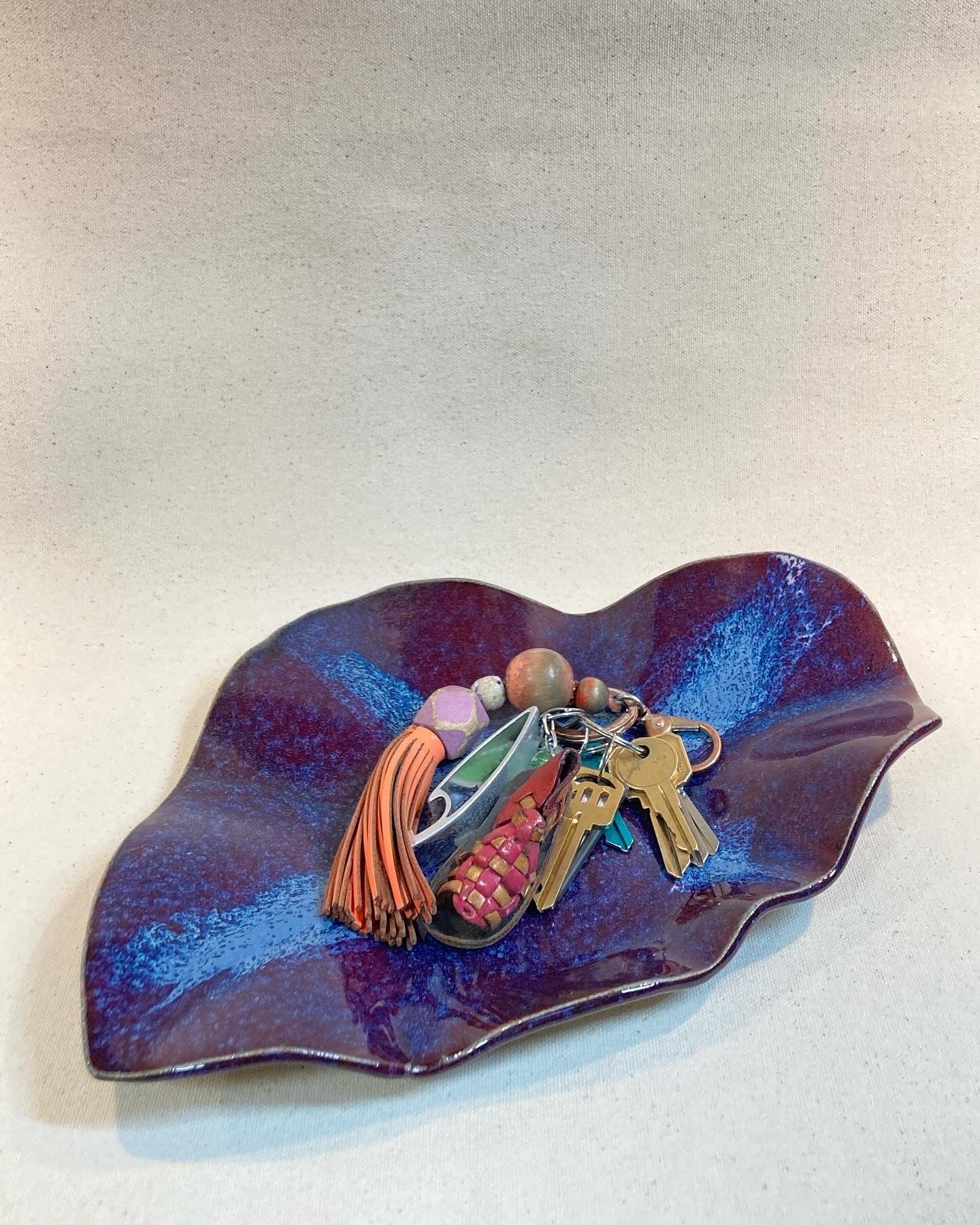 Decorative purple and blue ceramic dish with keys and a tassel on a white background