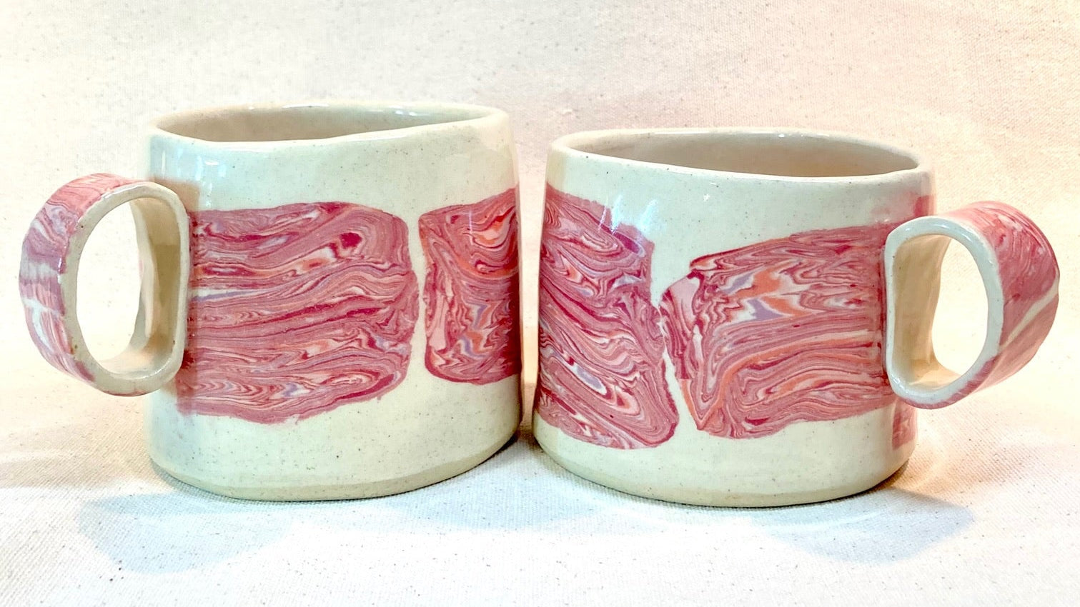 Two ceramic mugs with pink and red nerikomi layered stripe design on a canvas background